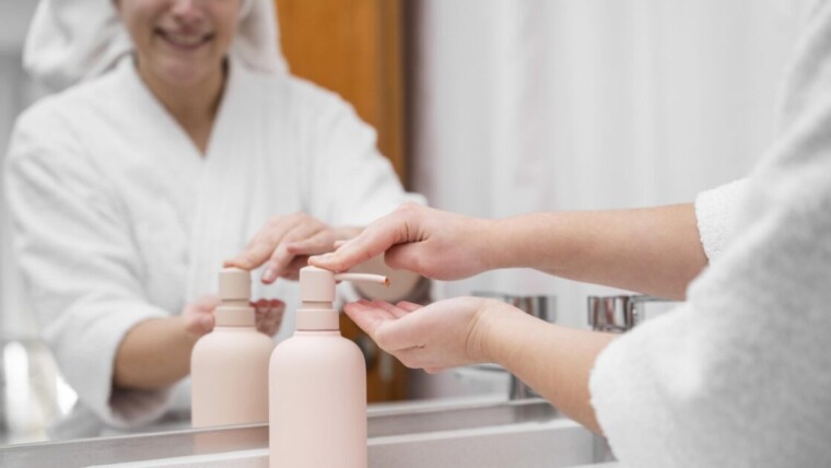 Hotel guest's hands operating pink refillable shampoo and conditioner dispensers, showcasing eco-friendly room amenities