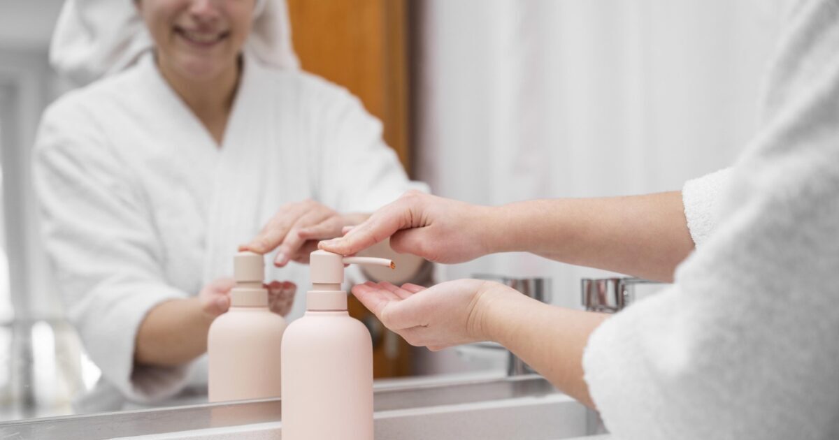 Hotel guest's hands operating pink refillable shampoo and conditioner dispensers, showcasing eco-friendly room amenities